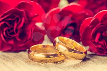 Wedding rings with red carnations on wooden background