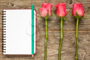 Three roses and blank notebook on a old wooden planks