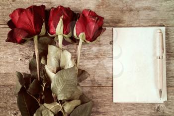 Faded roses and blank paper sheets with pen on wooden background
