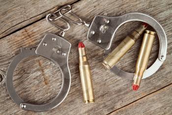 Metal handcuffs and dummy cartridges on the wooden background 