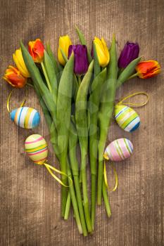 Easter eggs and colorful tulips bouquet on wooden background