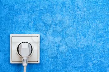 Electrical plug connected into the socket on blue wall