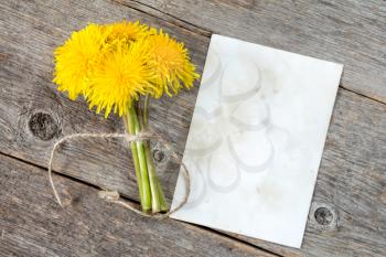 Bunch of dandelion flowers and blank card on wooden background