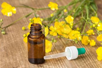Yellow wildflowers and small bottle with dropper on wooden background