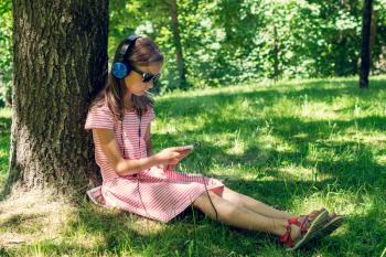 Girl listening to music under the tree shadow
