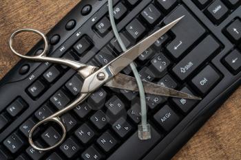 Scissor cutting internet cable over computer keyboard. Prevention of theft of data, information via the Internet.