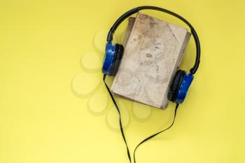 Audio books concept. Headphones put over  book with empty cover on yellow background, top view, copy space