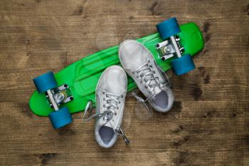 Child sneakers and overturned green skateboard lying on wooden background