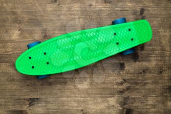 Green skateboard on wooden background, top view