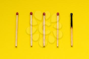 Wooden matches with one burned out on yellow background