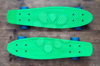 Two green skateboards on wooden background, top view