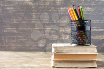 Stack of books with pencil cup on wooden background