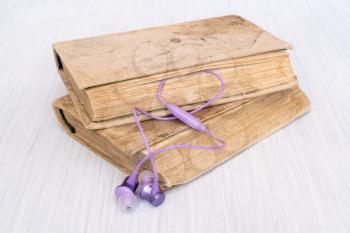 Audio book concept. Purple earphones and books on wooden table. 