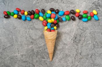 Wafer horn with colored candy on a stone background. Top view, copy-space.