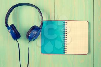 Stereo headphones and blank notebook on wooden background 