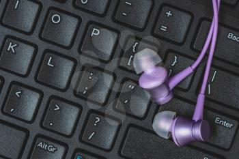 Purple audio earphones on the black keyboard. Listening music concept