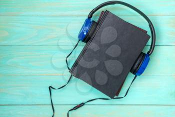
Audio books concept. Headphones put over hardback book with empty cover on blue  wooden background, top view, copy space