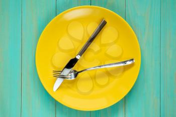 Empty yellow plate with fork and knife
