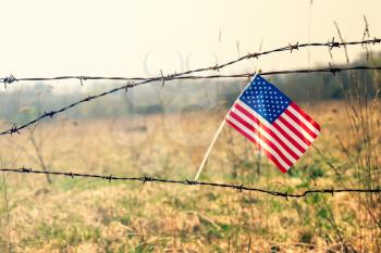 American flag on old barbed wire fence. Borders protection,social issues on refugees or illegal immigrants