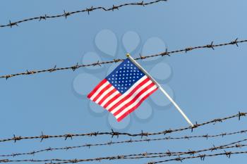  American flag on old barbed wire fence with blue sky background. Borders protection,social issues on refugees or illegal immigrants
