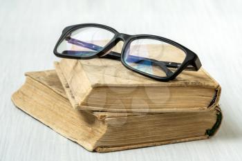 Eyeglasses on stacked books placed on white wooden background