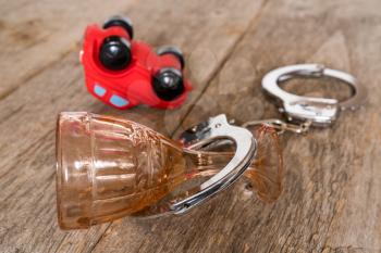 Concept of a drunk driving accident. Overturned car, alcohol glass and handcuffs