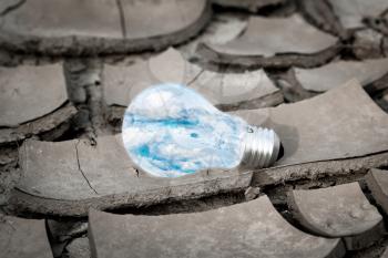 Save energy concept. Sky and clouds inside light bulb lying on the  cracked dry soil