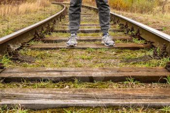 Man walking along railway. Legs of traveler on rail tracks. 