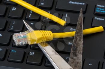 Scissors cutting  network cable over computer keyboard. Internet connection disconnected. 