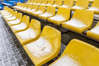 Stadium seats in the snow in winter. Snow-covered yellow plastic  seats at the stadium in winter. Snowfall interferes with sports. Uncleaned stadium.