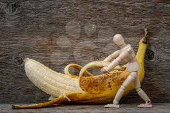 Wooden doll peeling a banana. Diet and nutrition concept.