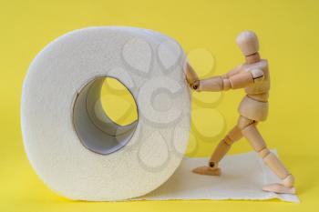 Wooden man pushes a roll of toilet paper. Concept of the problem with digestion.