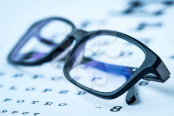 Modern reading glasses on a eye sight test chart. Blue toned image.