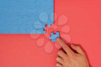Hand putting the last piece of blue jigsaw puzzle on red background.Finishing complicated project, solution, triumph.