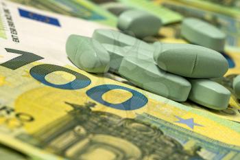 Green medicine pills or capsules over euro banknotes