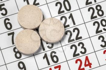 Three medical tablets on a monthly calendar. Medication plan, schedule, list or calendar concept.