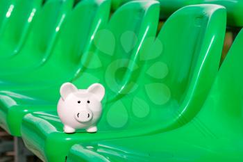 Piggy bank on the green seats of sports ground.  Concept of sport fund. Money and sport.