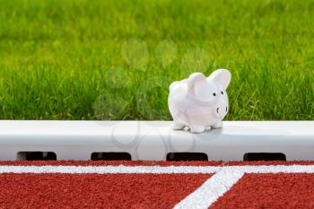 Piggy bank on the running track in the stadium.  Concept of sport fund. Money and sport.