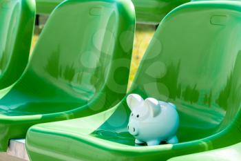 Piggy bank on the green chairs of sports stadium. Sports and money.