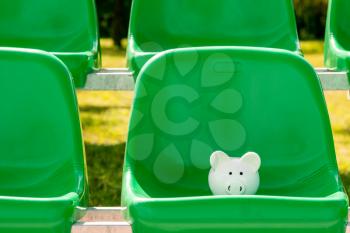 Piggy bank on the green plastic chairs of sports stadium