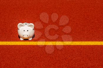 Piggy bank on the yellow starting line in the stadium. Copy space.