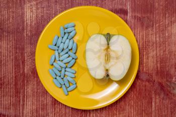 Drawing up a diet. Pills in a plate with an apple half on a wooden table.  Healthy eating, diet, lifestyle concept.