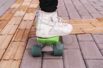 Close-up of feet of girl in sneakers standing on skateboard on pavement