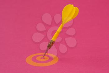 Yellow dart arrow hitting in the yellow target center on the pink background