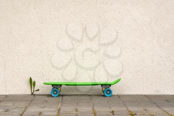 Green plastic skateboard on the pavement against white wall. Copy space.