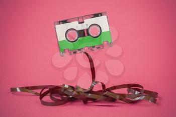 Audio cassette with pulled out tape on a pink background