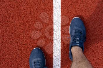 A man in running shoes stands at the stadium on the track . The athlete is preparing for the competition. 