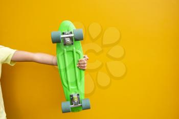 Youth culture. Hand with green penny board against  yellow urban wall with empty space for text