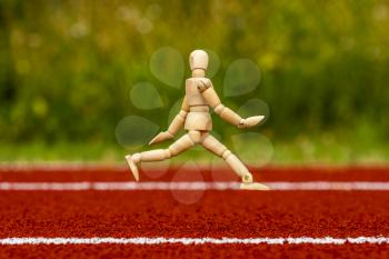 Wooden man  running on the stadium track with rubber surface