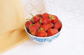 Dishes with ripe, red strawberries on the table with a white cloth on a background of beige and white shades